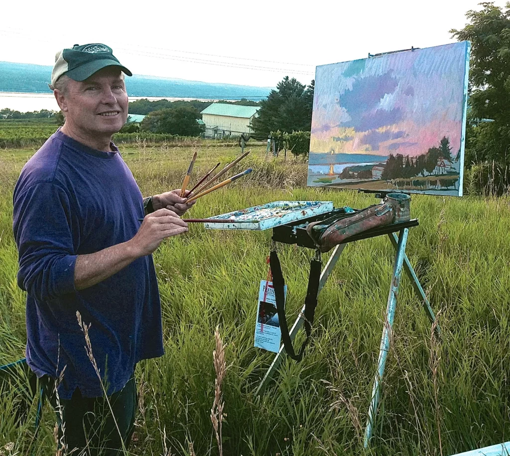 A photo of Brian S. Keeler, smiling at the camera, standing in front of a canvas in a field.