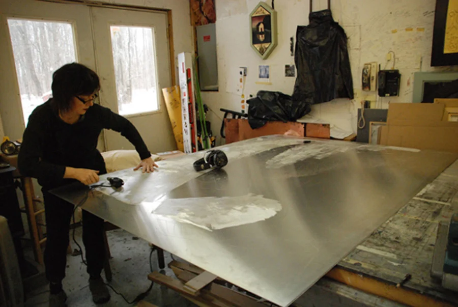 A photo of artist Treacy Ziegler, stood over a metal table top.